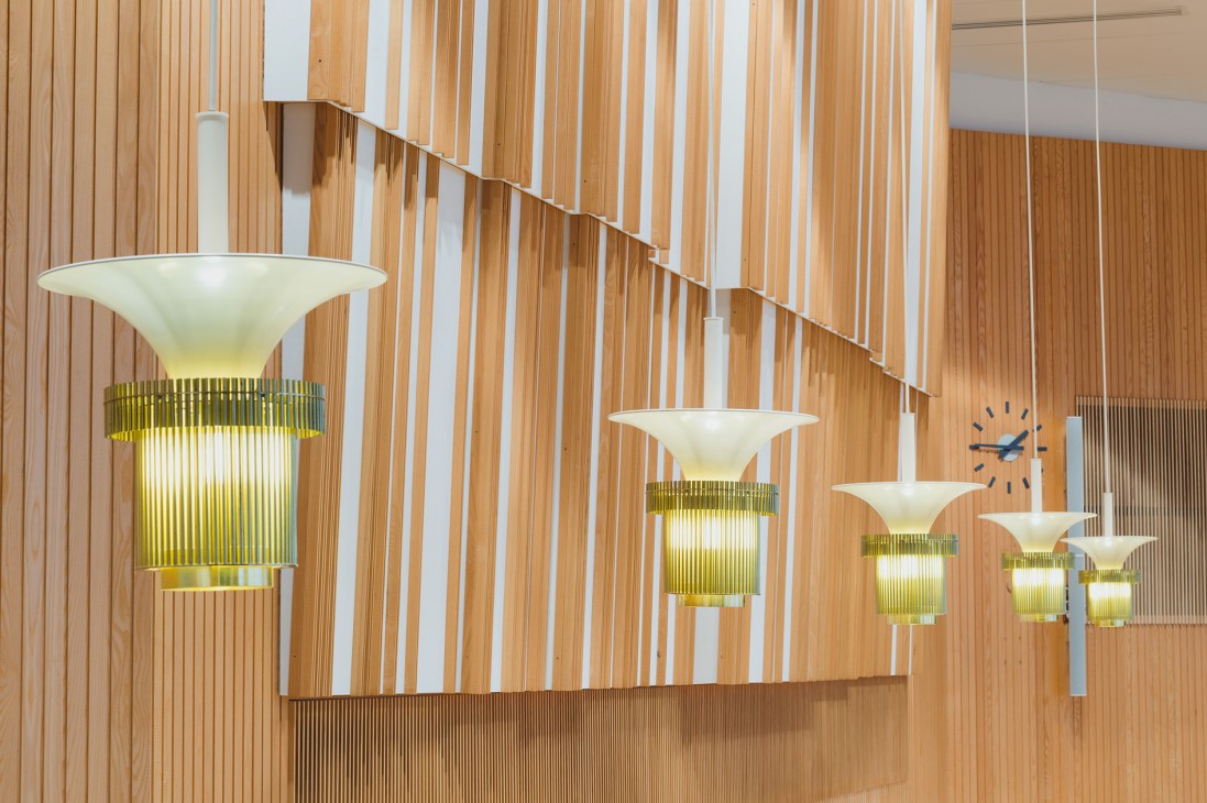 Pendant lamps with brass ribbed shades hanging in a wooden-panelled interior with white vertical slats.