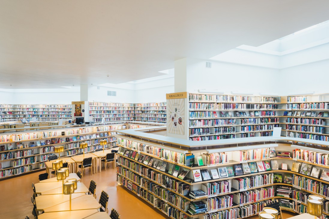 Interior of Rovaniemi Public Library with curved white ceiling, skylights, wooden bookshelves, and reading tables designed by Alvar Aalto.