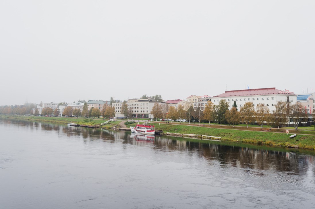 Rovaniemi's riverfront cityscape viewed from Jätkänkynttilä Bridge, showing Soviet-era apartment buildings and a red riverboat.