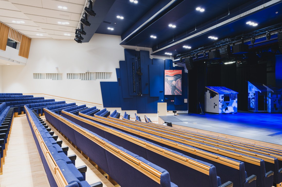 Interior of Rovaniemi Theatre in Lappia Hall showing rows of blue seats and wooden railings facing a stage with blue lighting.
