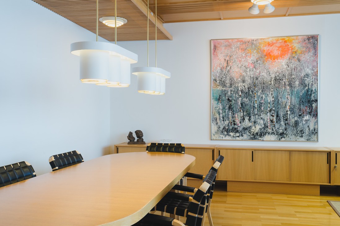 Modern meeting room with wooden table, pendant lights, and abstract painting at Rovaniemi mayor's office.