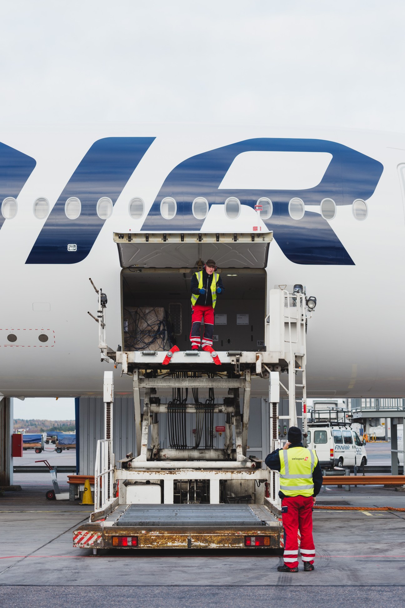 Finnair ground crew member in safety vest standing at open cargo door of Airbus A350 aircraft.