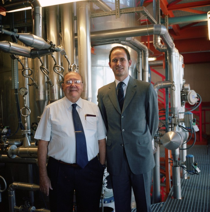Noel Micaleff and his nephew Christopher standing in an industrial facility with metal pipes and equipment.