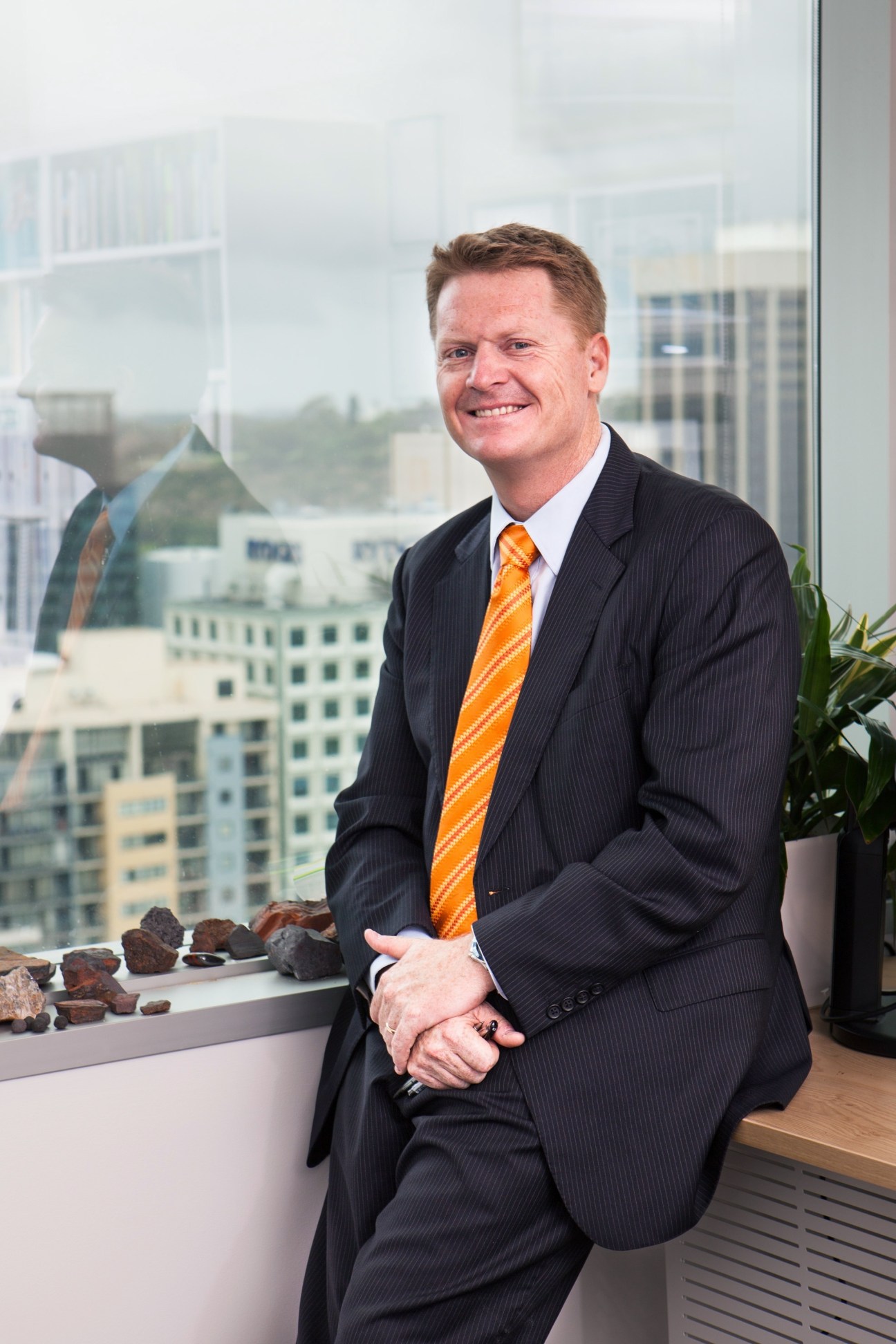 David Flanagan, founder of Atlas Iron, sits by a window with iron ore samples displayed on the sill behind him.