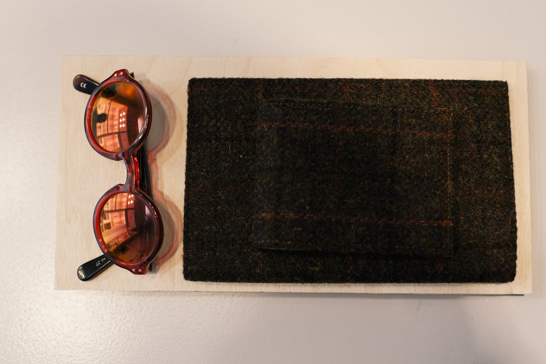Red tortoiseshell-framed glasses and dark textured fabric displayed on light wood surface.