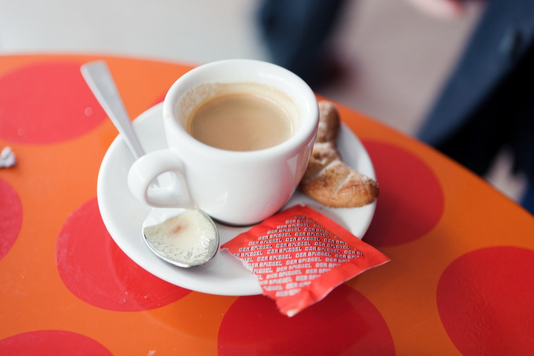 Coffee cup with saucer and Der Spiegel branded sugar packet on colorful orange and red table.