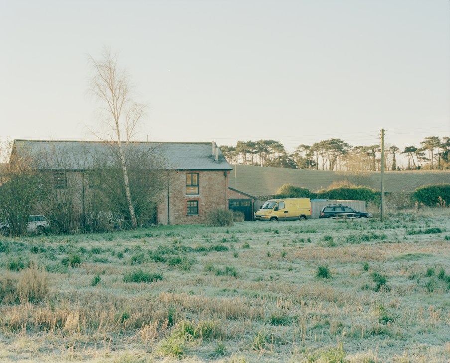Stone cottage workshop with slate roof in rural Devon countryside, yellow van and car parked outside.