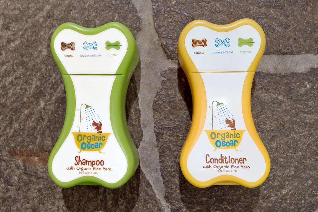 Two bone-shaped bottles of Organic Oscar pet shampoo and conditioner with aloe vera in green and yellow packaging.