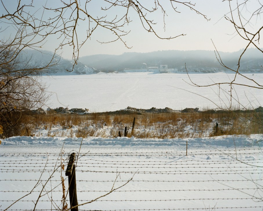 Frozen Amur River with bare branches in foreground, Chinese town of Heihe visible across the ice in winter.
