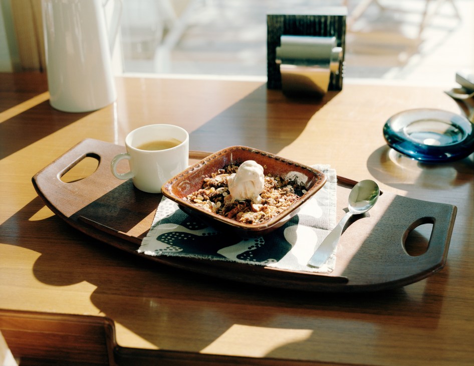 Apple crumble dessert with vanilla ice cream served with tea on a wooden table.