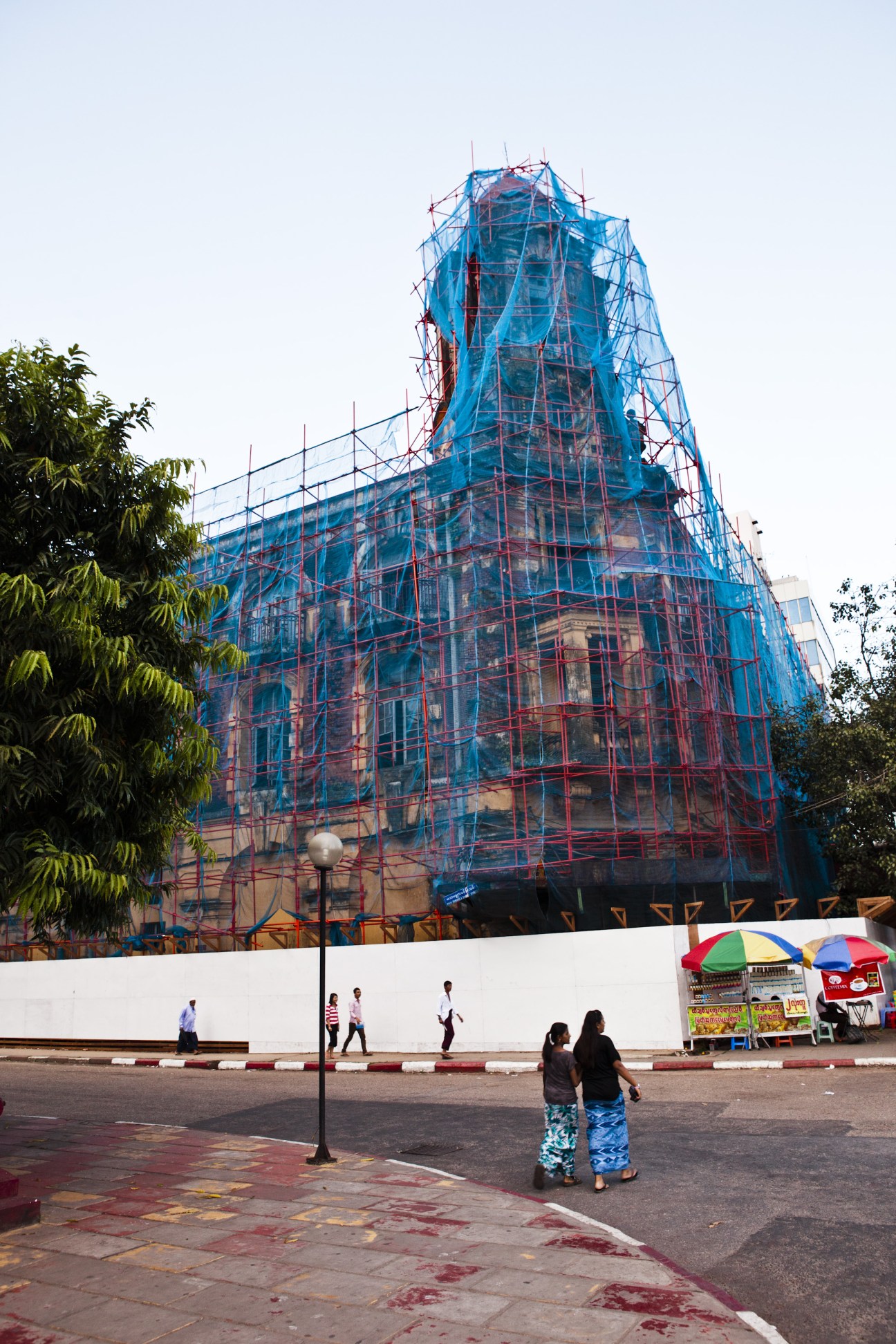 Colonial building under restoration with blue and red scaffolding covering its facade in Rangoon.
