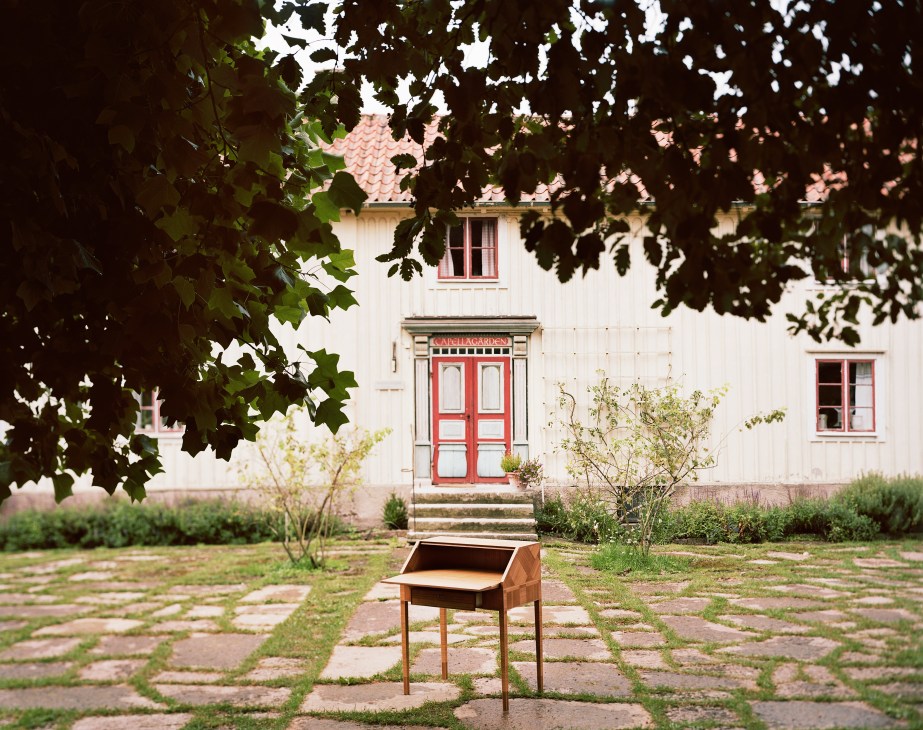 Wooden desk displayed in a courtyard in front of a white building with red doors at Capellagården.