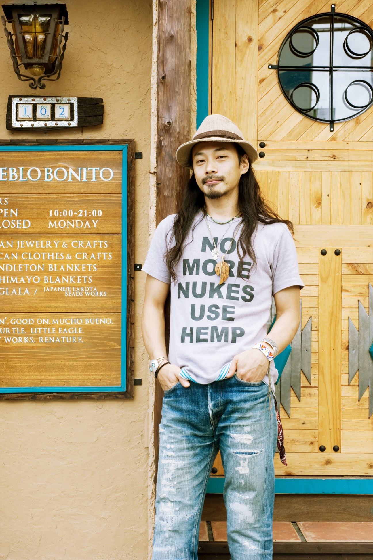 Masaru Tateuchi, owner of Pueblo Bonito clothing shop in Naha, stands outside his storefront wearing a hat and graphic t-shirt.