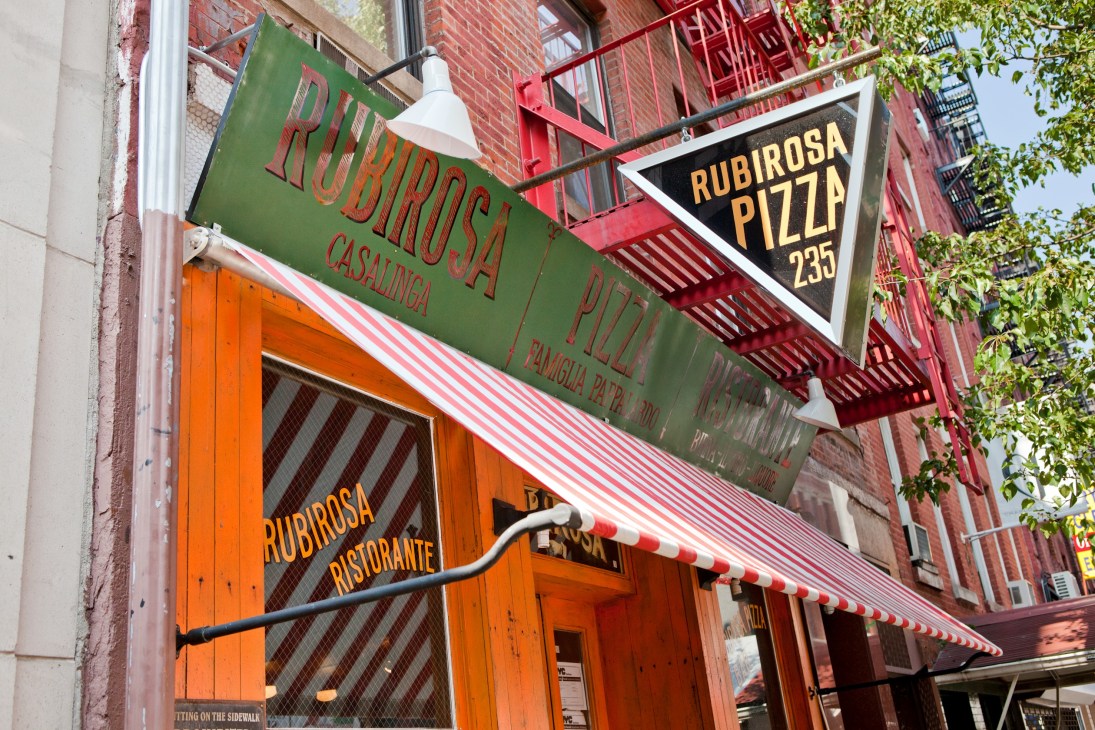 Rubirosa Pizzeria storefront with green and black signage and orange door on Manhattan street.