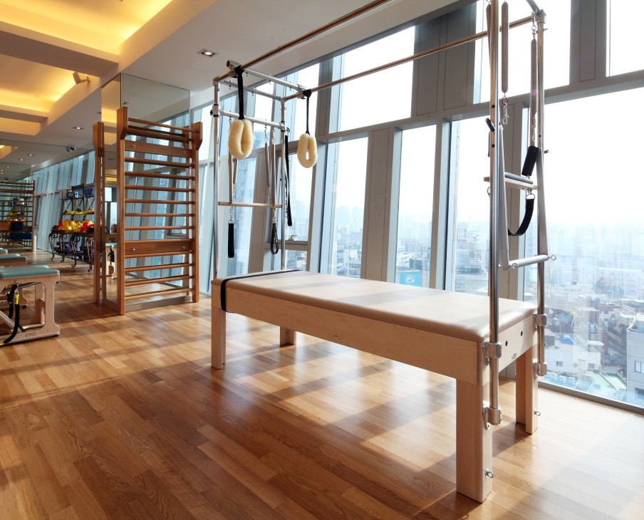 Modern pilates studio with wooden reformer equipment overlooking Seoul cityscape through floor-to-ceiling windows.