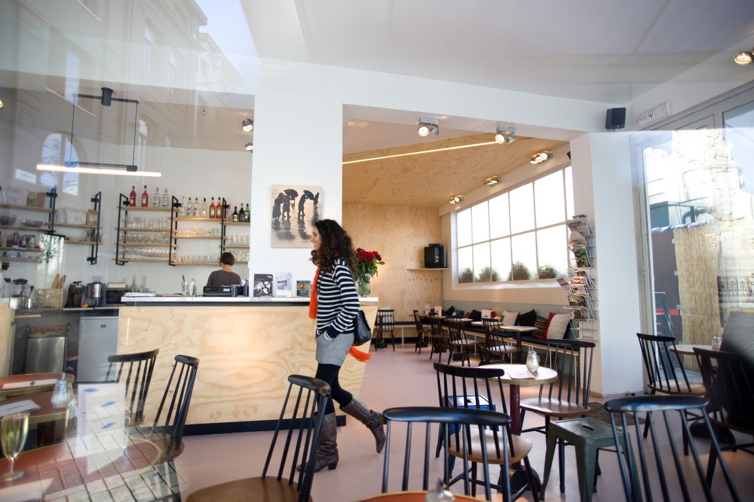 Interior of Vitrin café in Antwerp with wooden counter, bar seating, and dining area with black chairs.
