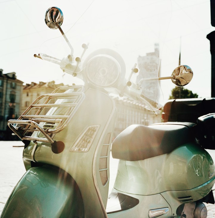 A cream-colored Vespa scooter with brass mirrors parked in Piazza Vittorio Veneto, Turin.