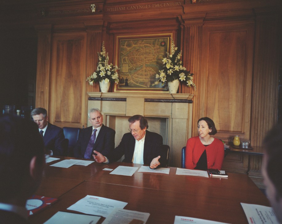 George Ferguson seated at a formal wooden conference table with three other professionals in an ornate wood-paneled room.
