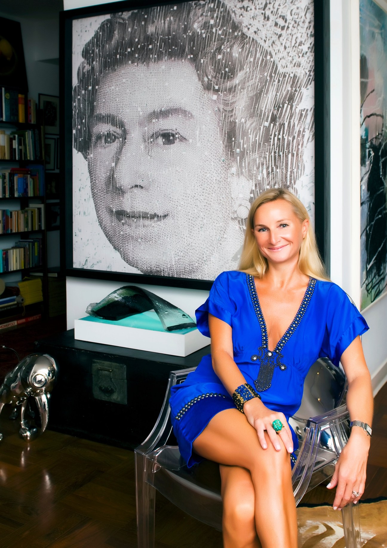 Woman in blue dress sitting in gallery with portrait artwork and sculptures behind her.