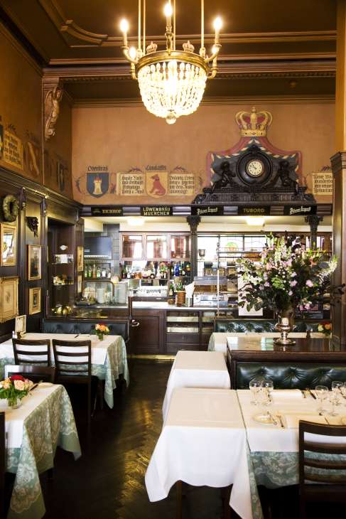 Interior of Kronenhalle restaurant in Zurich with elegant dining tables, crystal chandelier, and traditional beer hall decor.