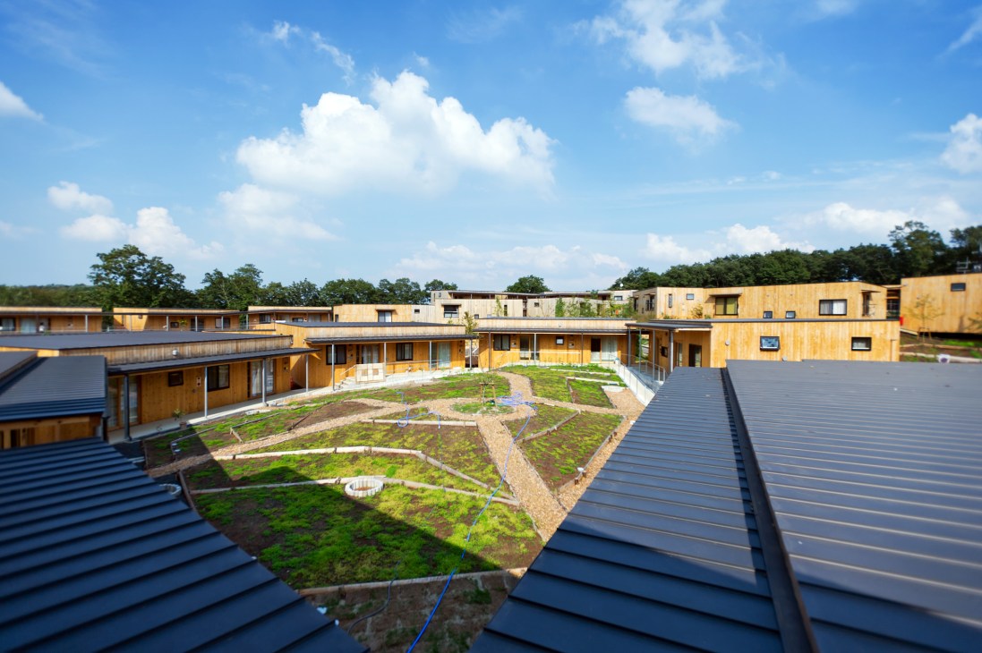 Aerial view of Yuimarl Nasu community in rural Japan showing wooden residential units clustered around a shared courtyard with gardens and green spaces.