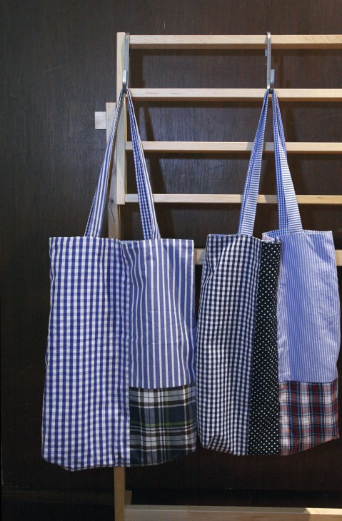 Morikage Shirt cotton fabric bags in various blue, black and checkered patterns hanging on a wooden rack.