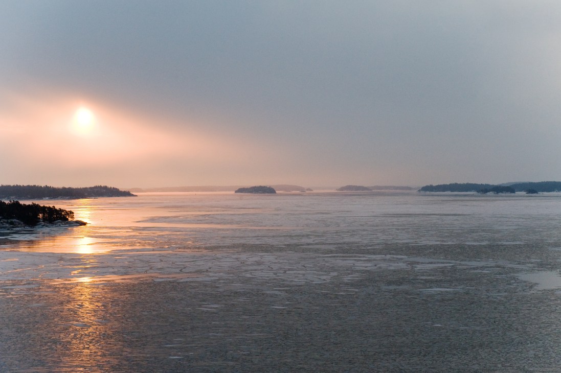 Sunrise over calm water with forested islands in the Stockholm archipelago.