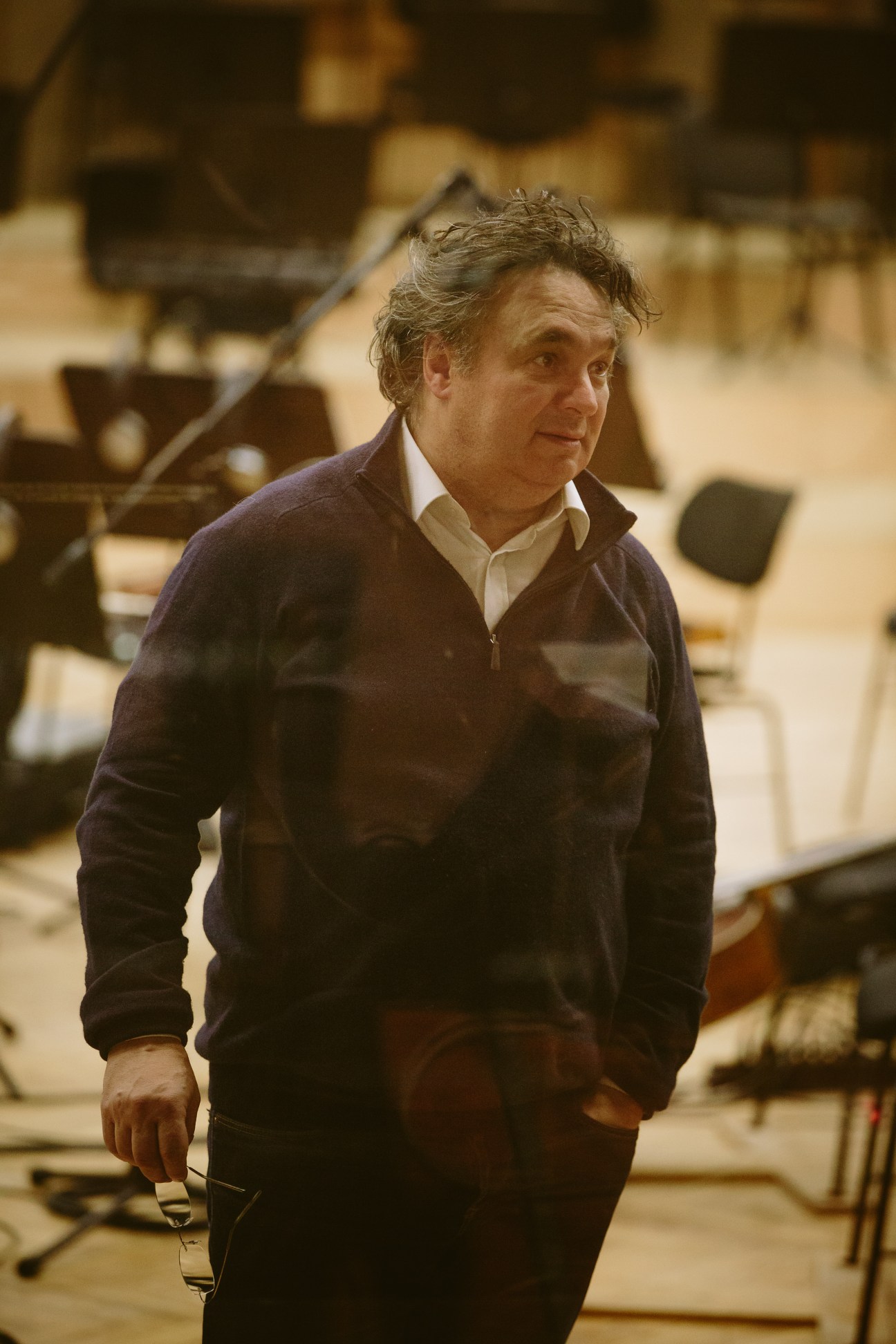 Conductor Tore Aas stands in a recording studio wearing a dark cardigan over a white shirt.