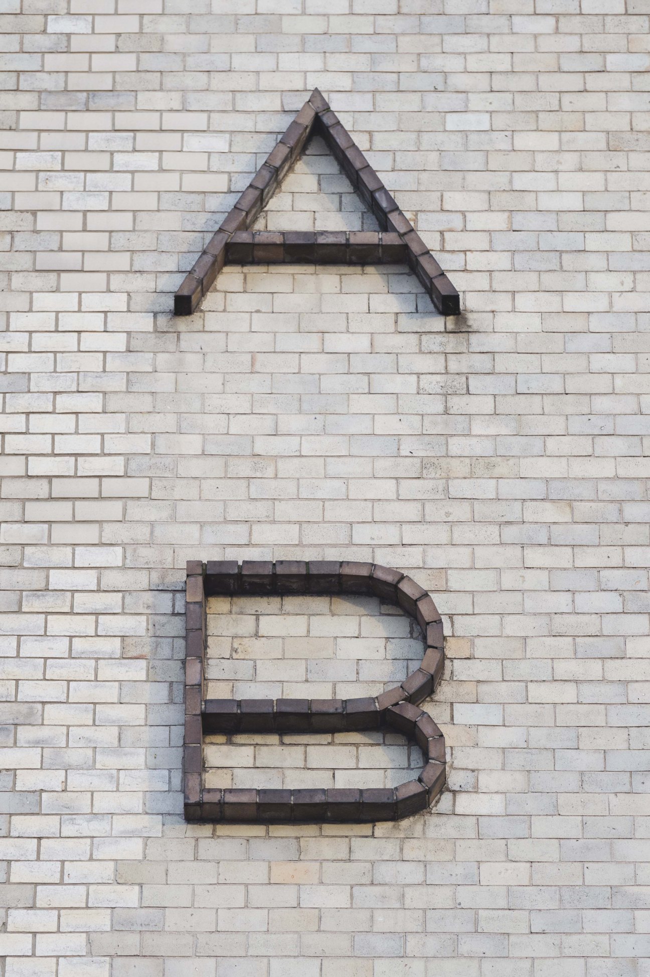 Brick letters forming the letter A mounted on a light brick wall.