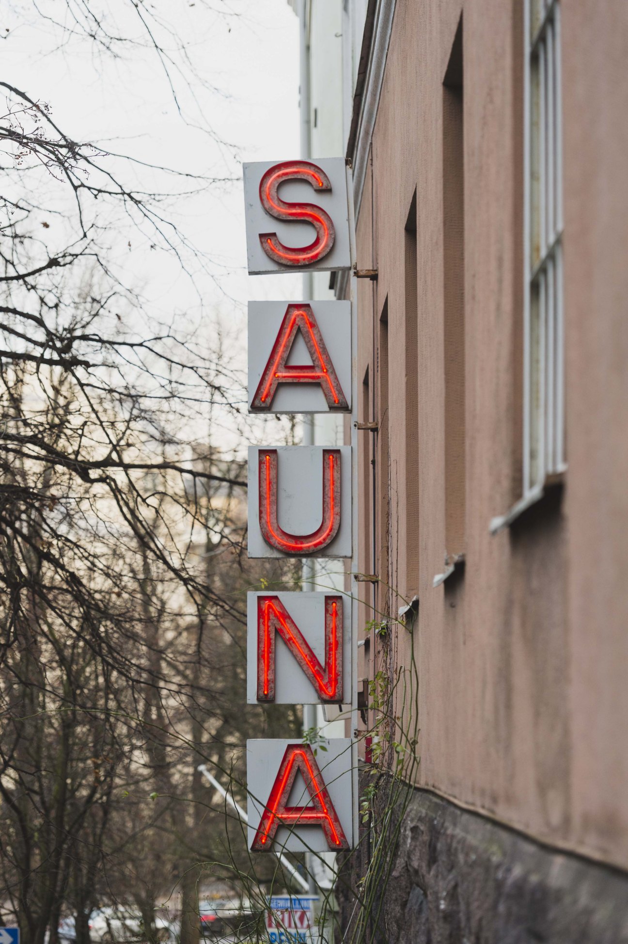 Vertical red neon sign spelling 'SAUNA' mounted on a brick building facade.