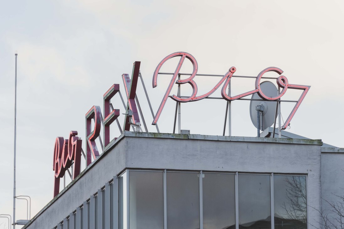 Bio Rex neon sign in red and pink tubes on a modernist building roofline.