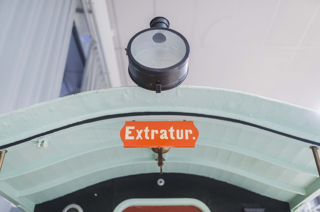 Vintage neon sign reading 'Extratur' in white letters on an orange rectangular background mounted on a light green curved tram structure.