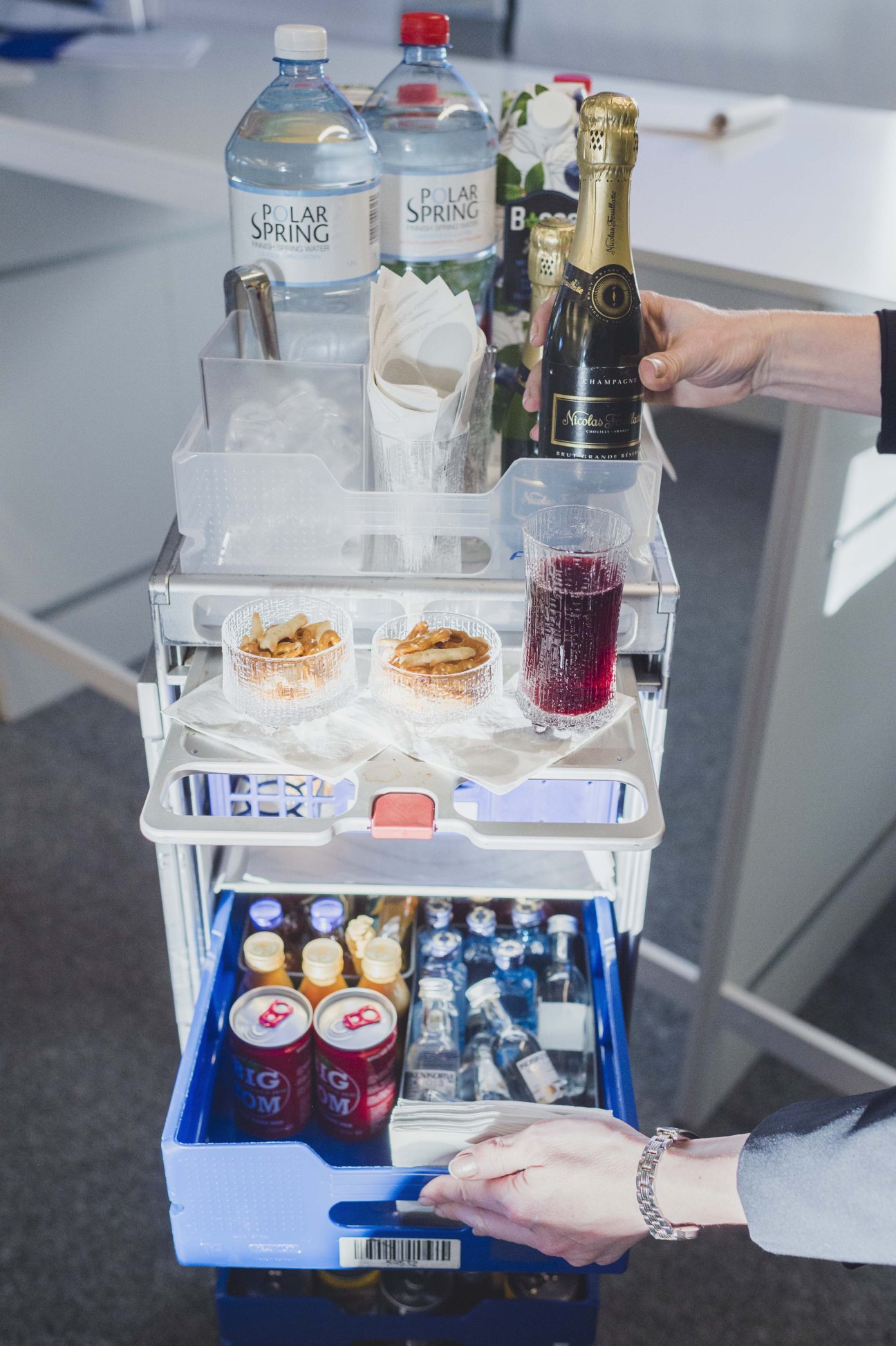 A tiered white service trolley stocked with Polar Spring water bottles, champagne, snacks, and beverages at Finnair Flight Academy.