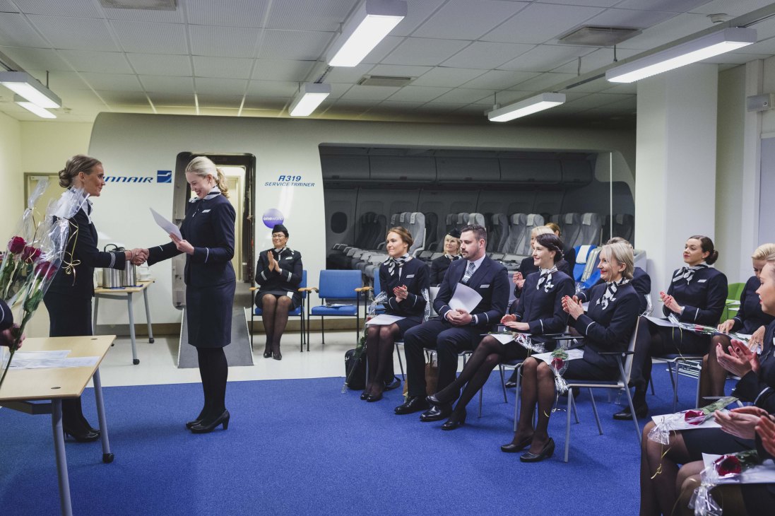 Finnair flight attendant trainees in dark uniforms seated in classroom during graduation ceremony at flight academy.