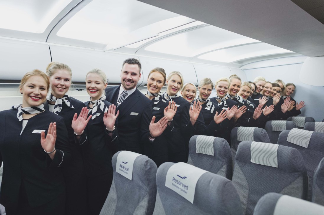 Finnair flight attendants in uniform waving inside an aircraft cabin with reserved seating.