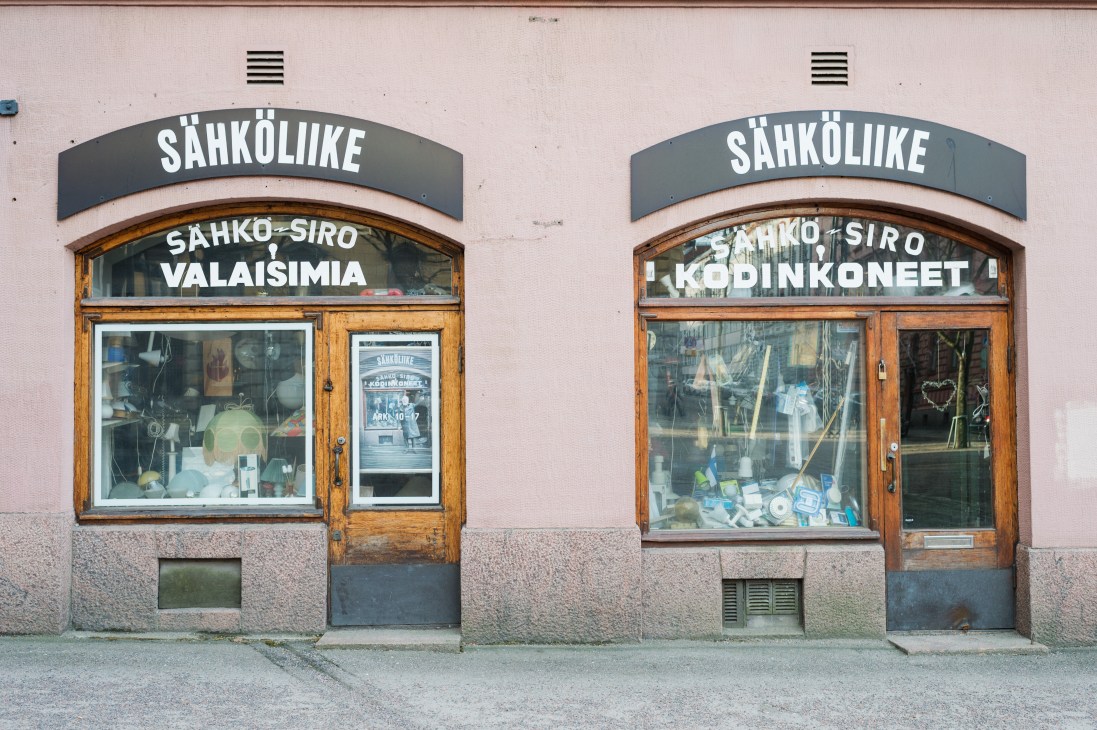 Two storefronts with wooden frames and Finnish signage on a pink building facade.