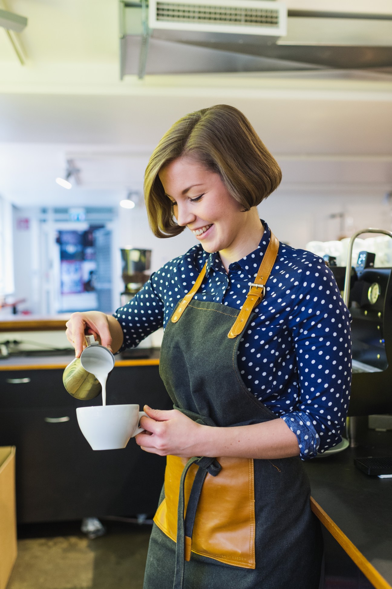 Sandra Halme pouring milk into a white cup at Kaffa Roastery in Helsinki.