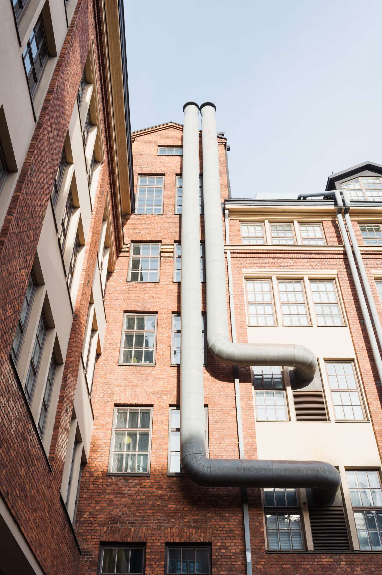 Red brick industrial building with white pipes and windows in Helsinki's Punavuori district.