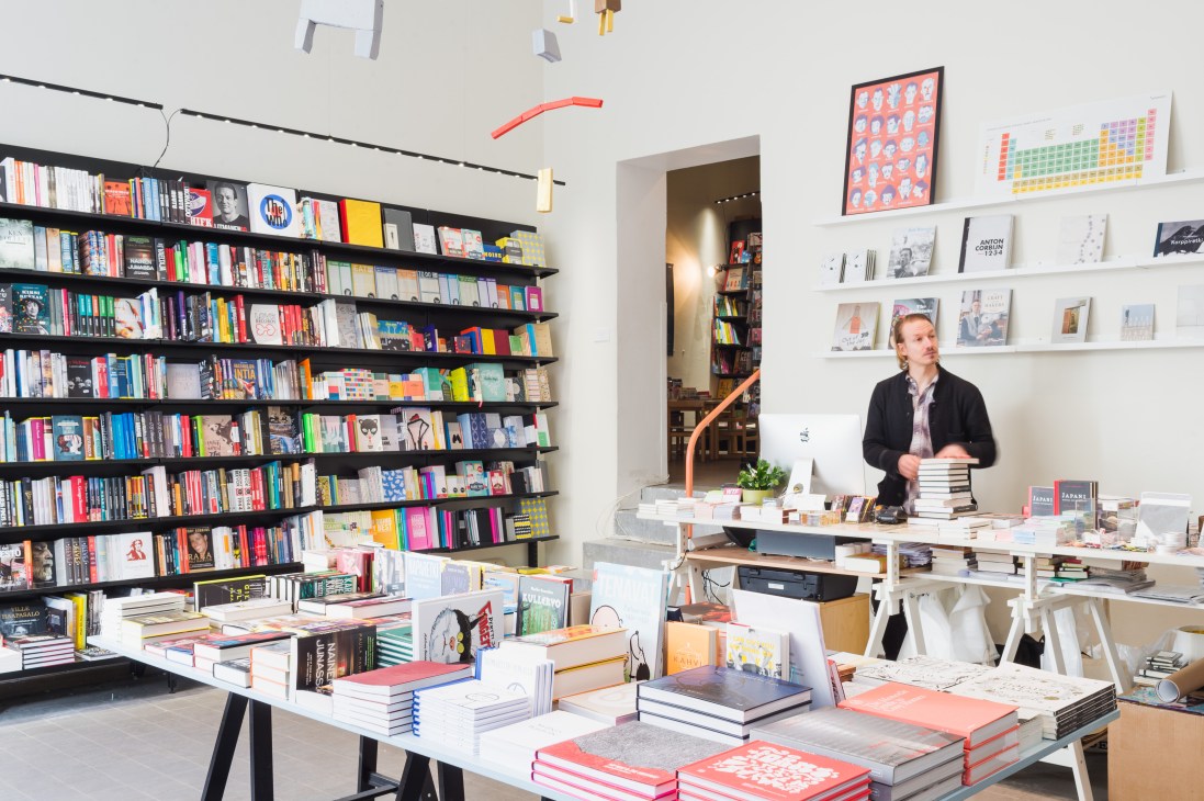Joose Siira stands in Nide bookshop surrounded by shelves and displays of books and art titles.