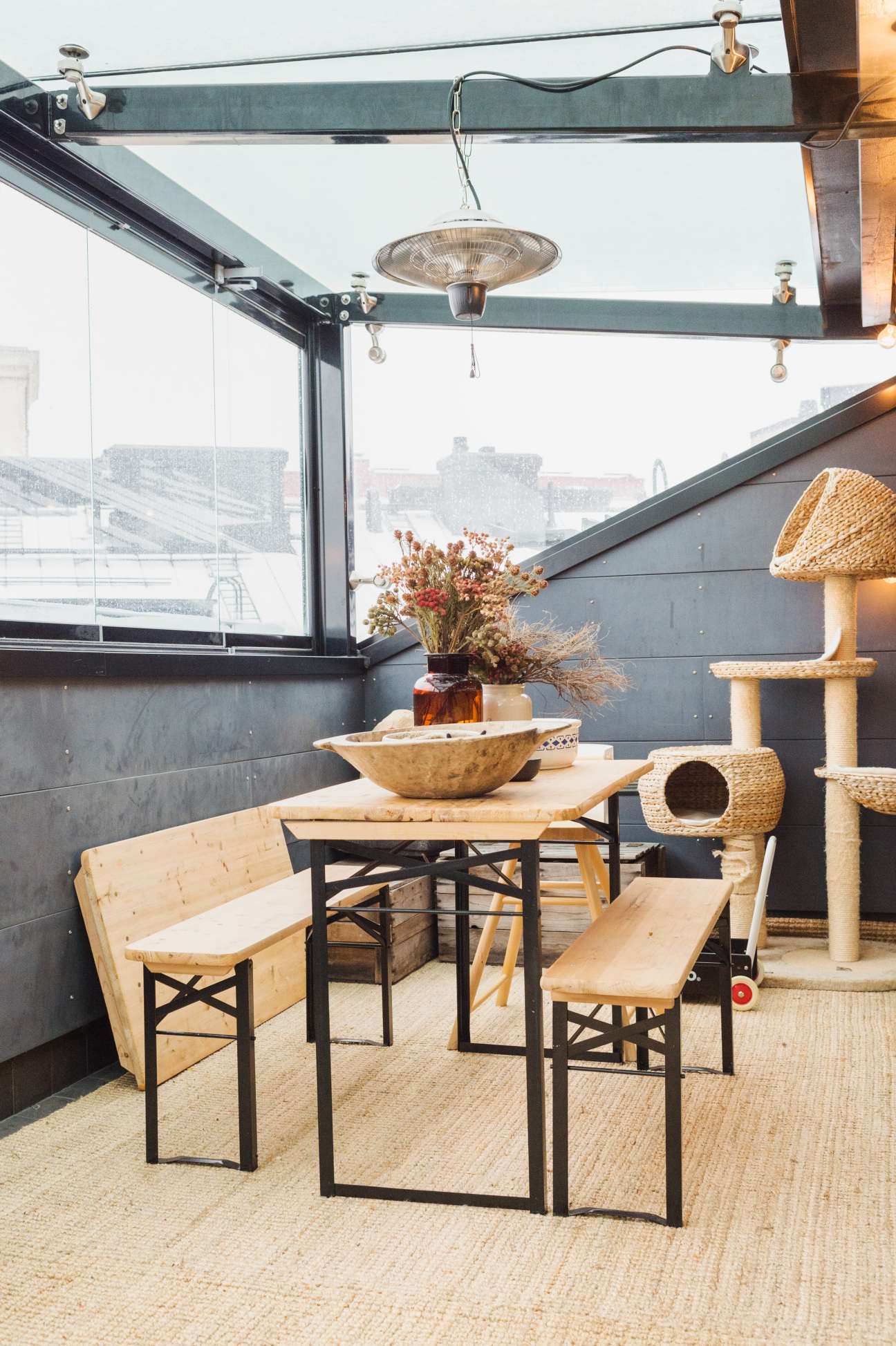 A modern roof terrace with wooden furniture, potted flowers, and a patio heater overlooking Helsinki.