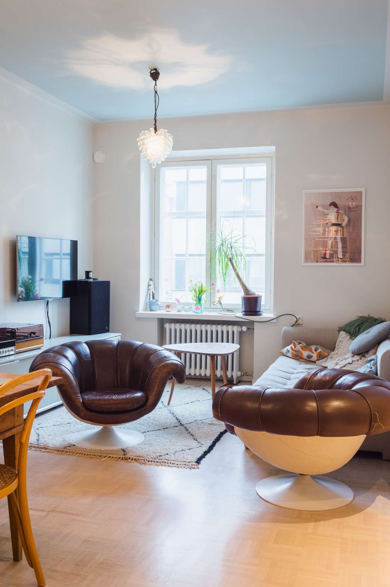 Modern living room with blue ceiling, leather chairs, pendant light fixture and large windows overlooking Helsinki.
