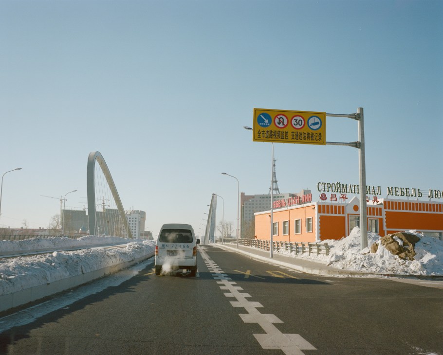 Vehicle entering Heihe across a modern bridge with yellow traffic sign and snowy landscape.
