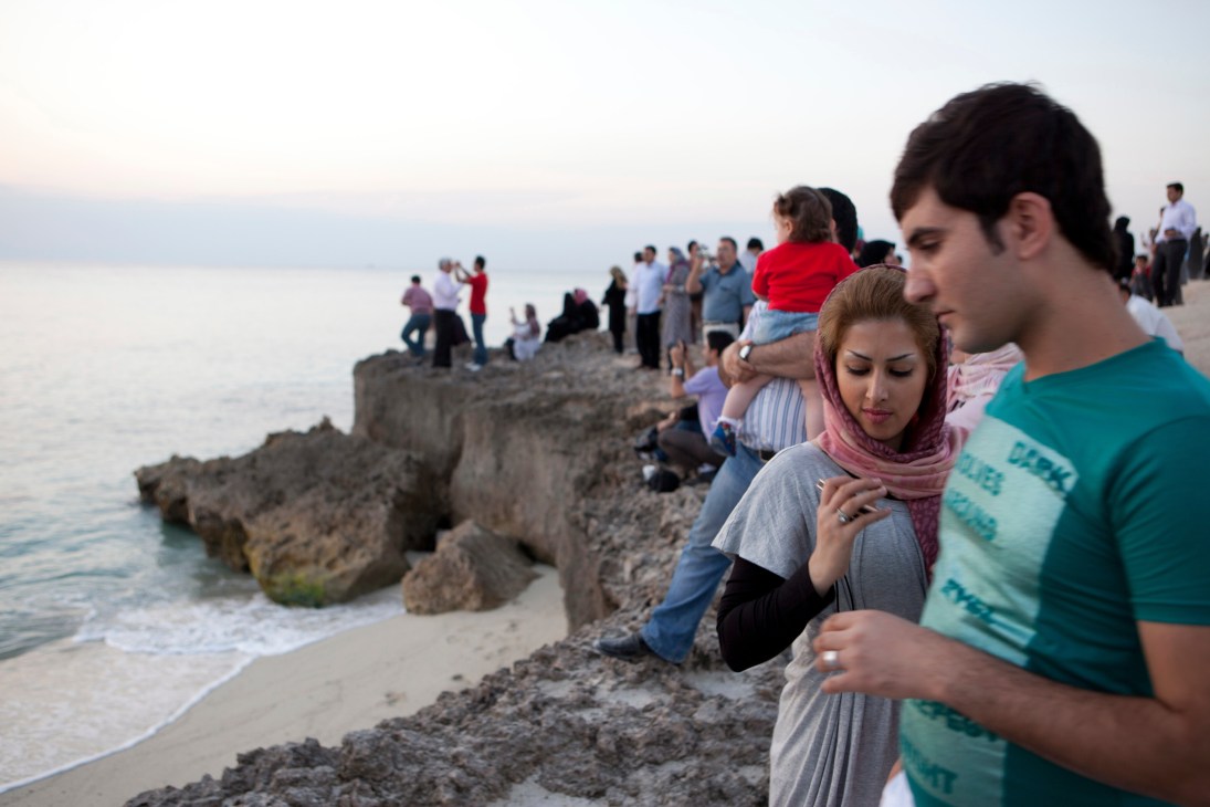 Couples and families gather on a rocky beach at sunset on Kish island, Iran.