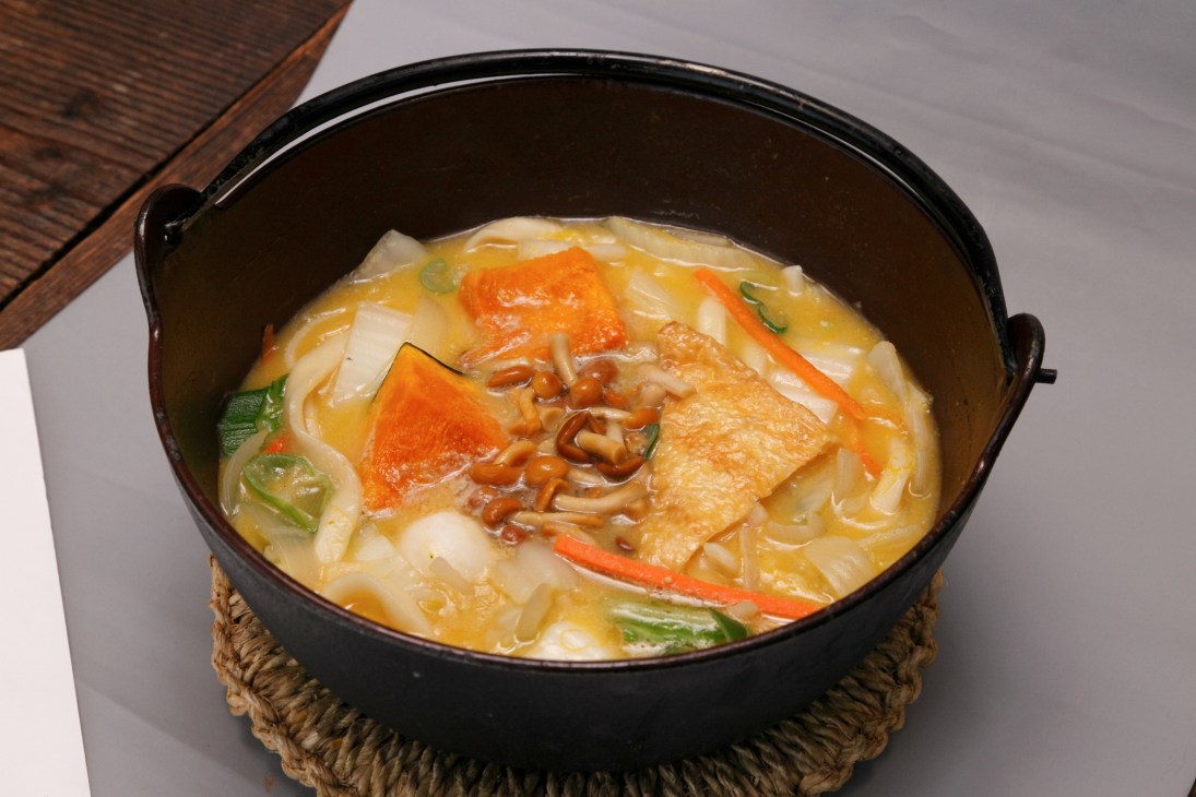 A black bowl of hoto noodles with vegetables and miso broth garnished with green onions
