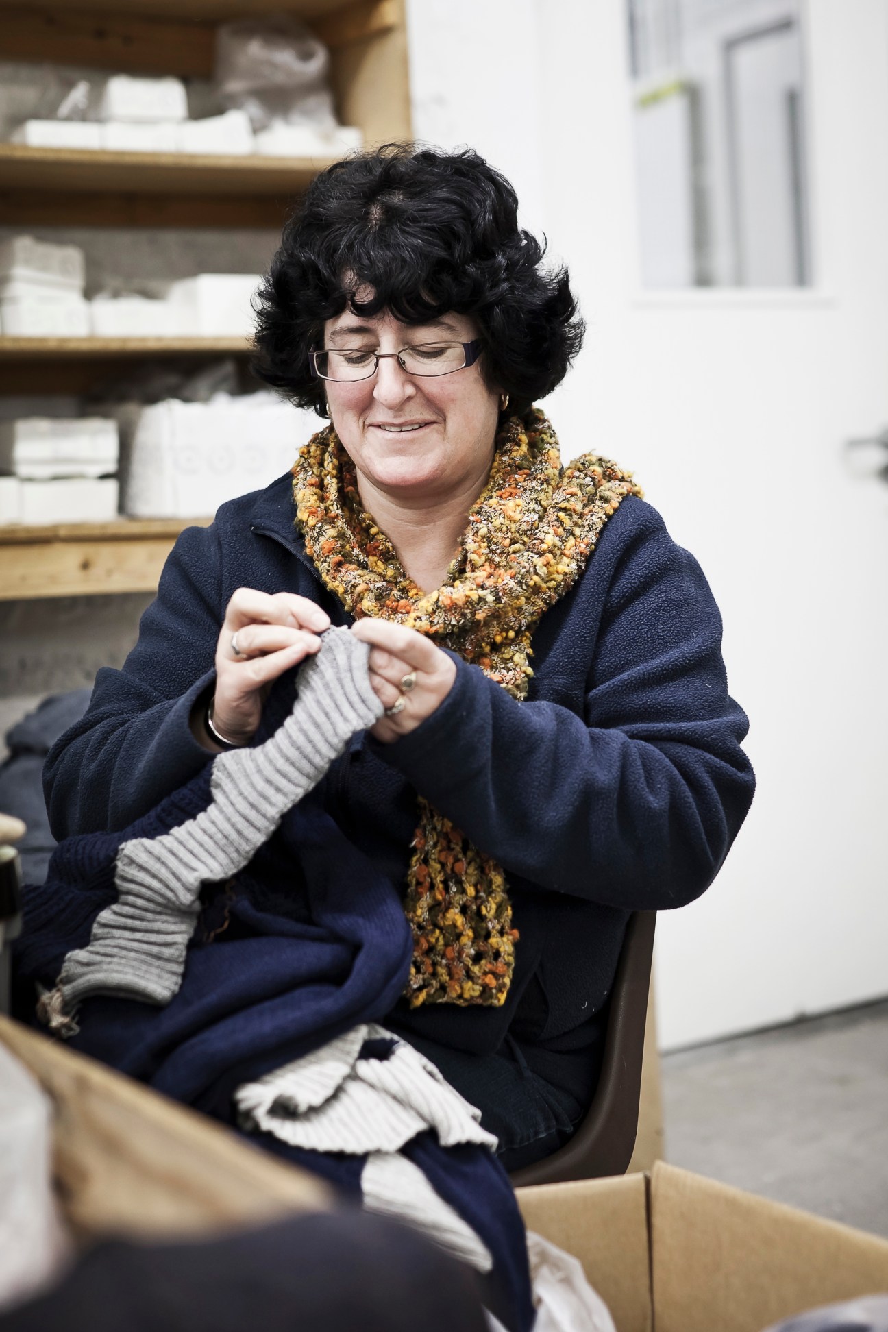 Woman holding handmade knitted garments in an Inis Meáin production workspace.