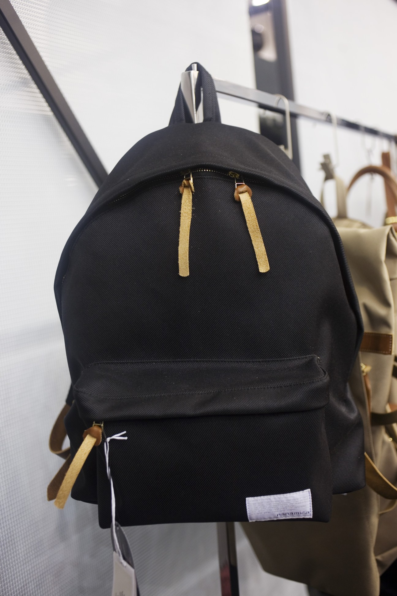 Black Nanamica daypack with tan straps displayed at Pitti Uomo menswear show.