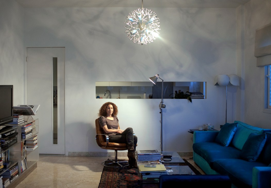 Woman sitting in brown leather chair in minimalist living room with blue sofa and modern pendant light.
