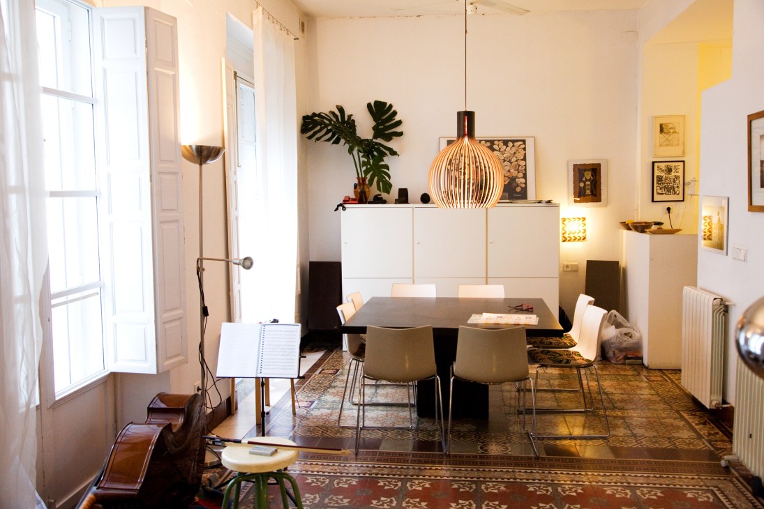 Bright modern dining room with white storage units, pendant lamp, artwork, and terracotta floor tiles.