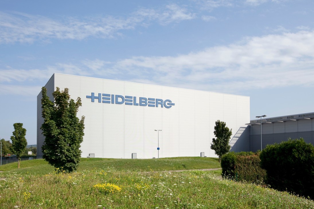 Modern white Heidelberg factory building with company logo, surrounded by green lawn and vegetation.