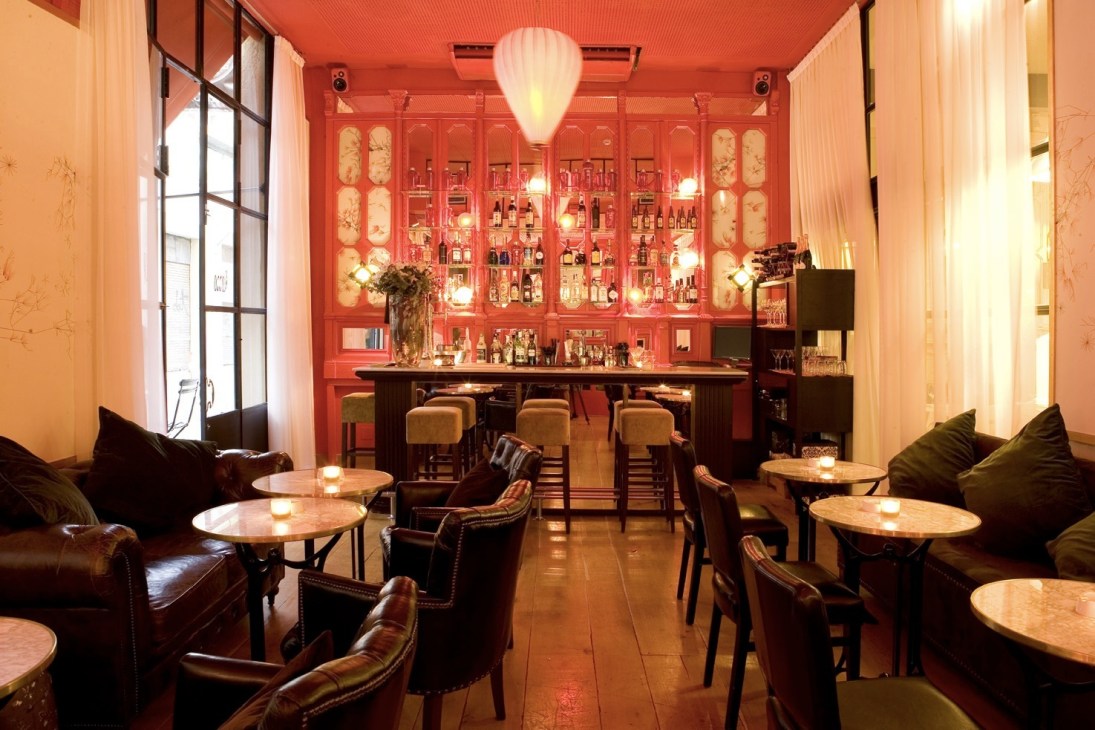 Modern bar lounge with red lacquered cabinetry, leather seating, and pendant lighting at an Andilana restaurant.